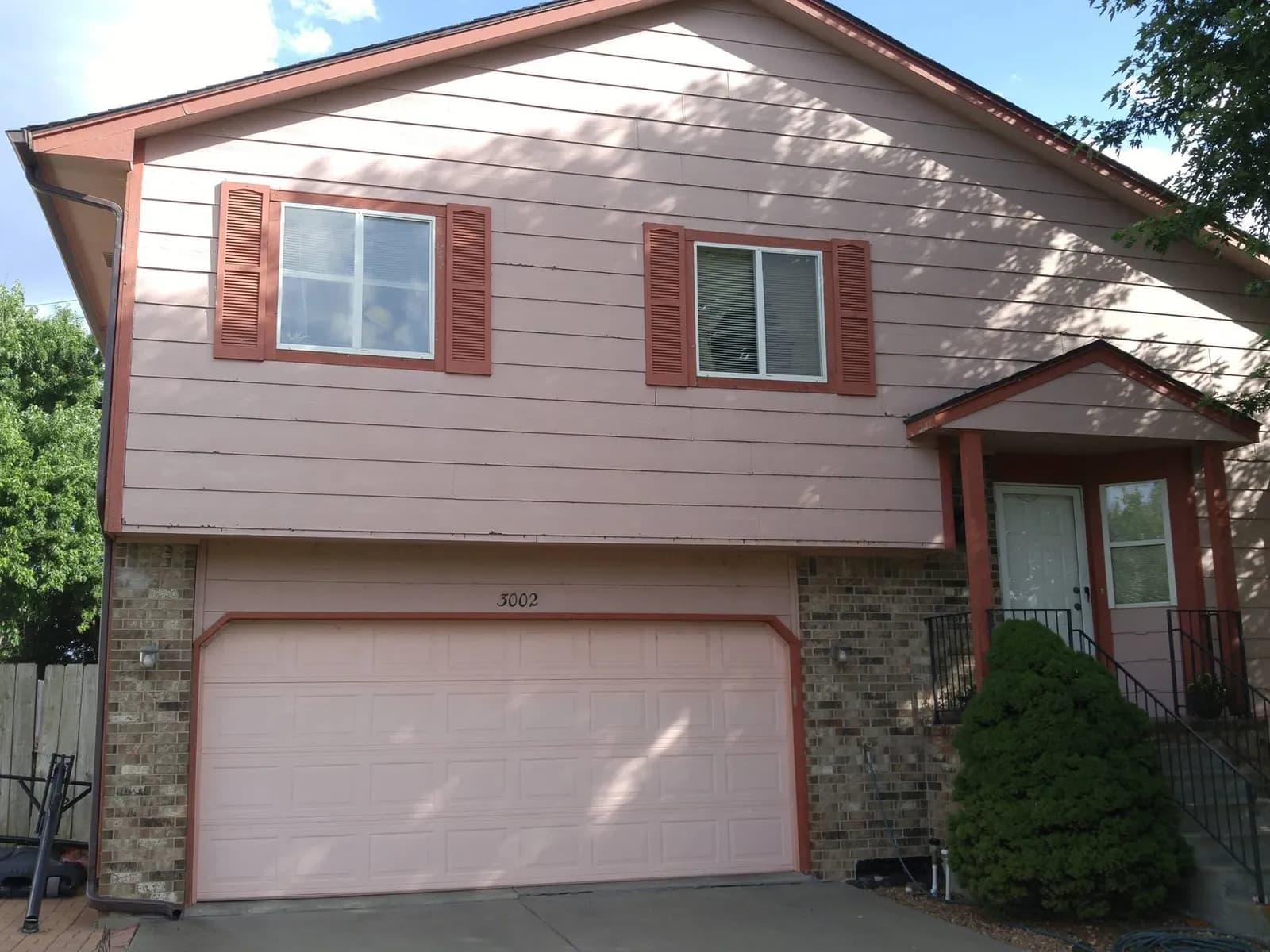 Brick split-level home before repainting, with dated salmon siding and terracotta shutters