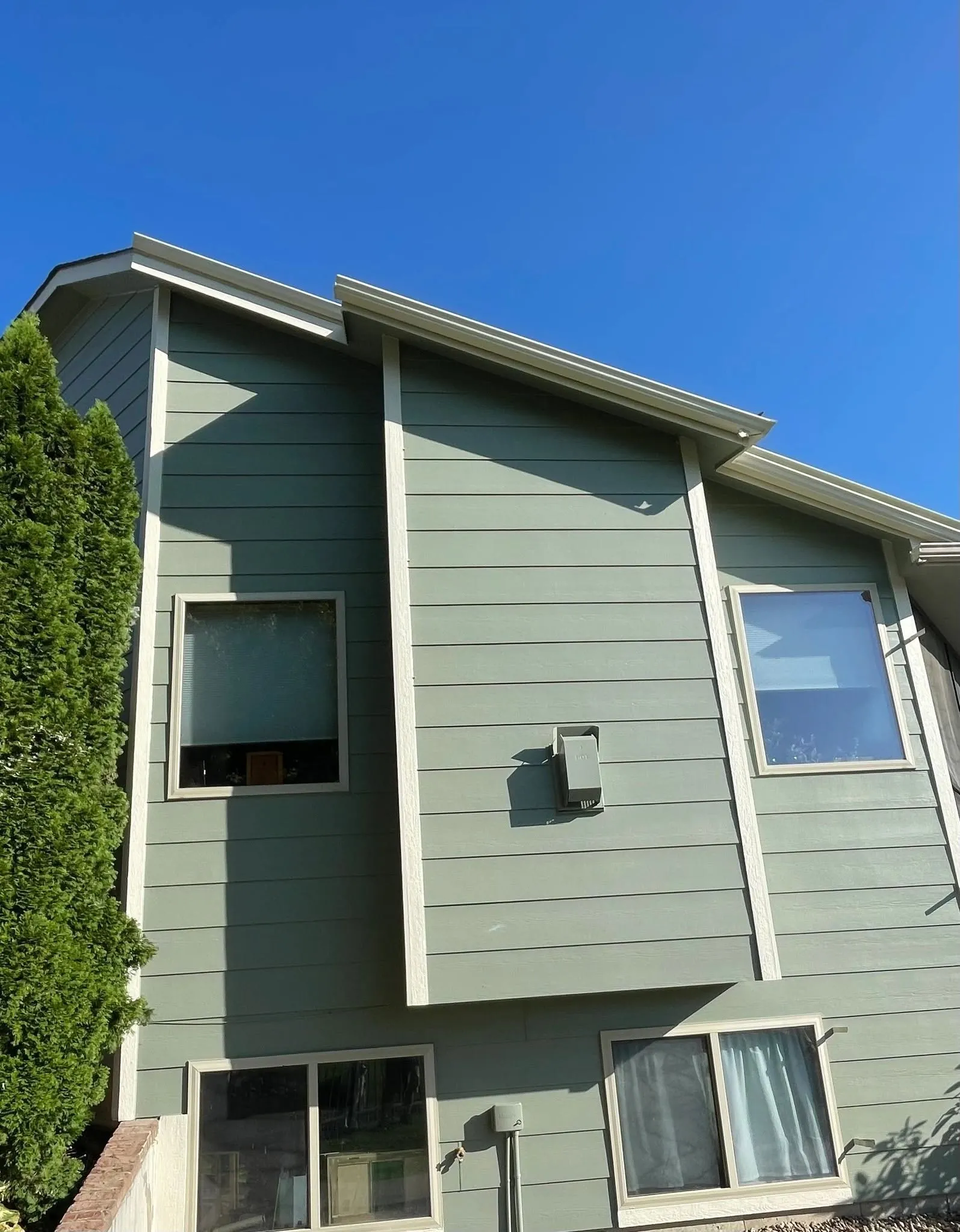 The same split-level home after repainting in sage green with crisp white trim