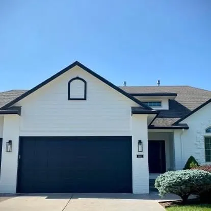 The same two-story home after repainting in white with a navy garage door and dark trim