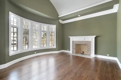 Freshly painted Wichita living room in sage green, with white crown molding, a bay window and a white fireplace surround